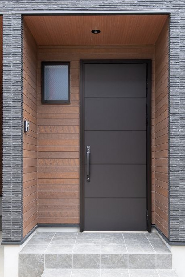 茶色の木調の壁にシンプルな黒茶の玄関ドア